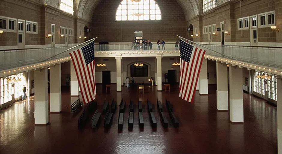 The restored Registry Room today: empty wooden benches on a polished tile floor, the same two flags, and a vaulted tile ceiling lit by arched windows
